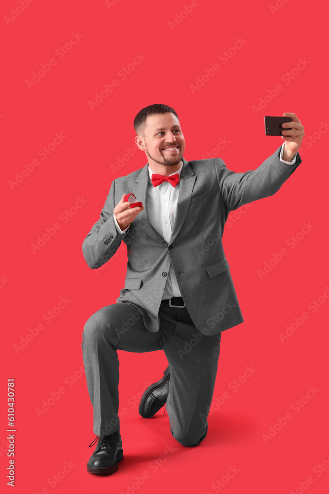 Handsome man with engagement ring taking selfie on red background