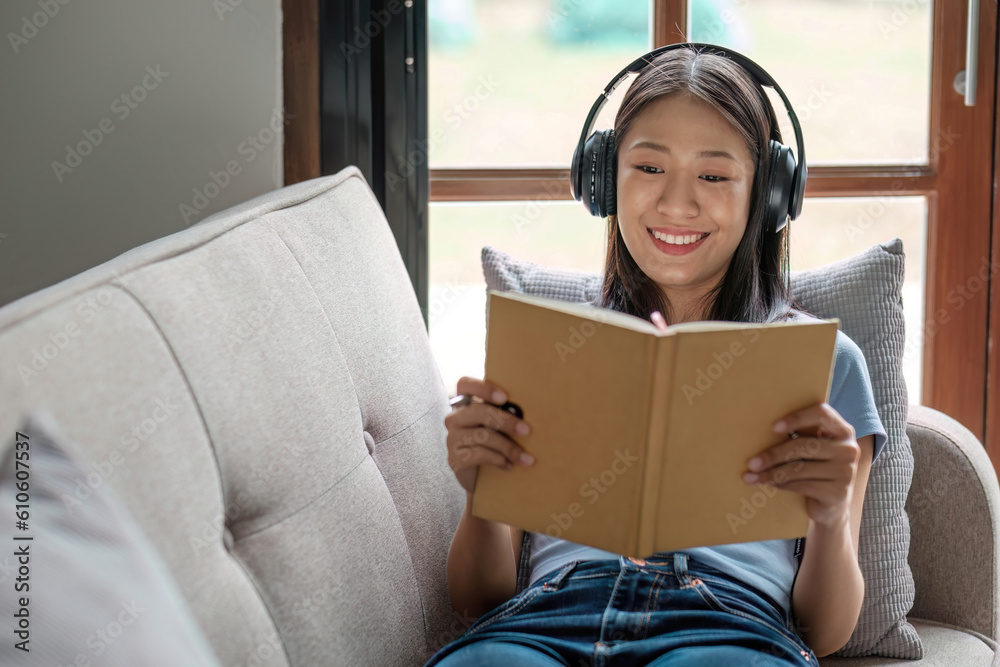 Young Asian woman listening music from headphones and writing note for her work idea in diary book.S