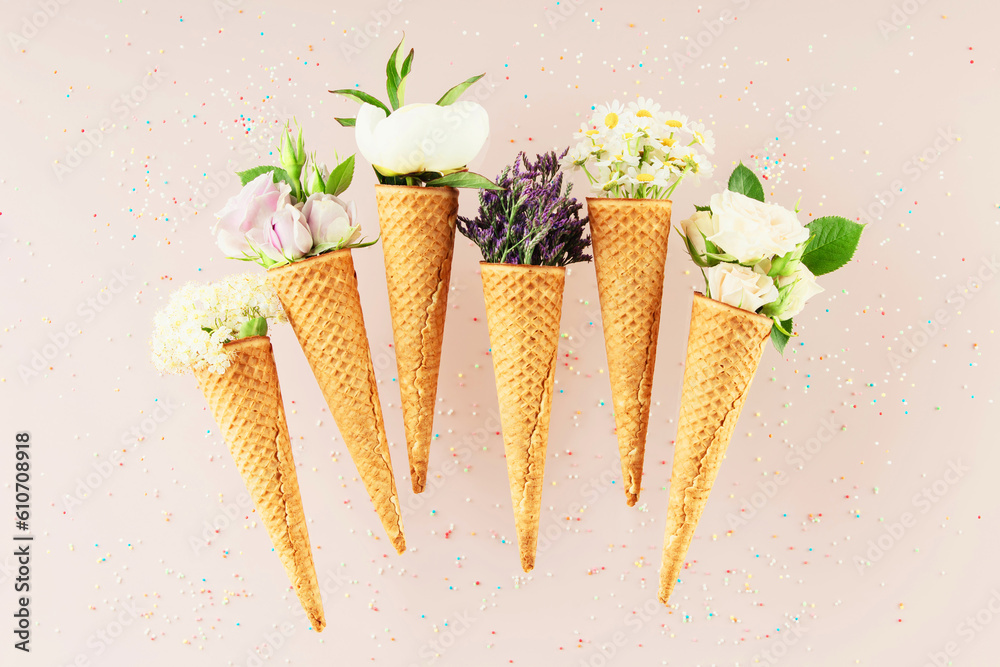 Flat-lay of waffle cones with flowers over pastel light pink background, top view