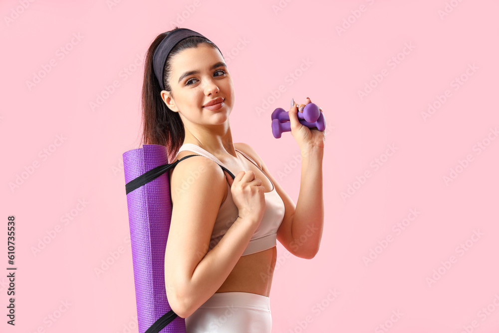 Sporty young woman with dumbbells and mat on pink background