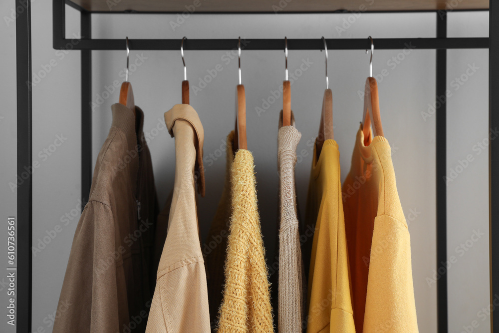 Rack with stylish clothes near light wall, closeup