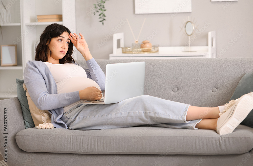 Tired young pregnant woman working with laptop on sofa at home