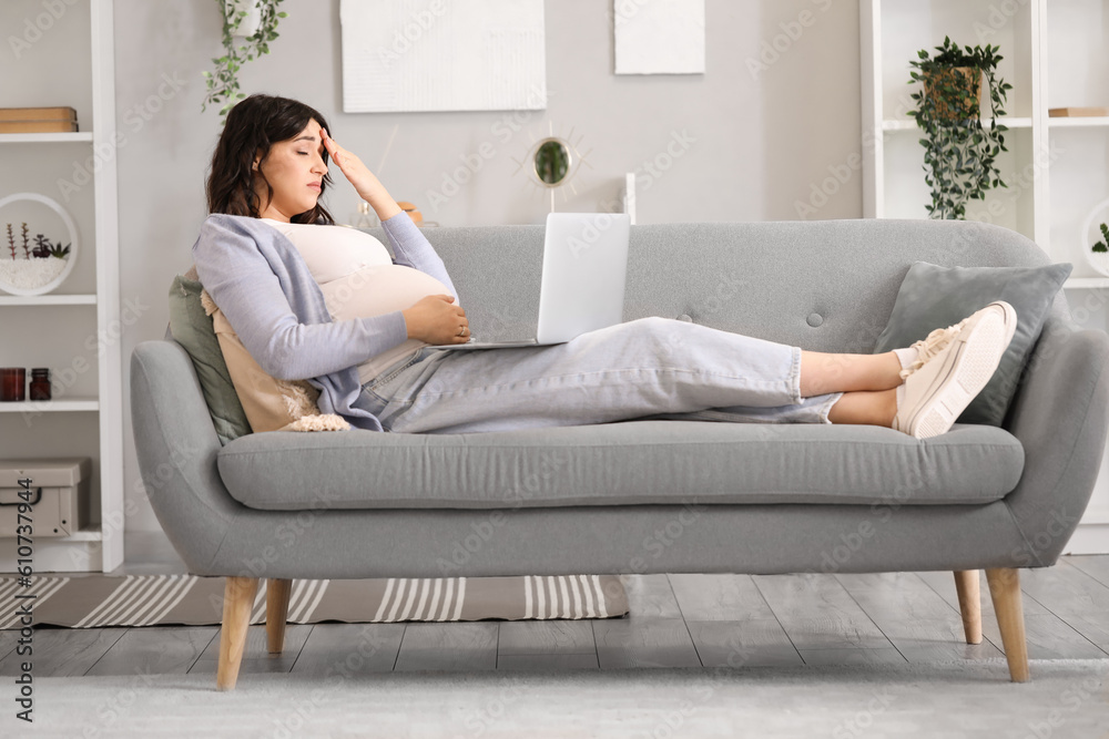 Tired young pregnant woman working with laptop on sofa at home