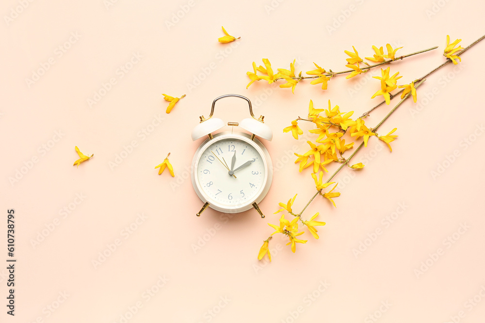 Blooming tree branches with yellow flowers and alarm clock on beige background