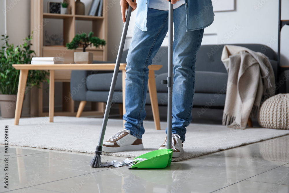 Young man sweeping floor with broom at home