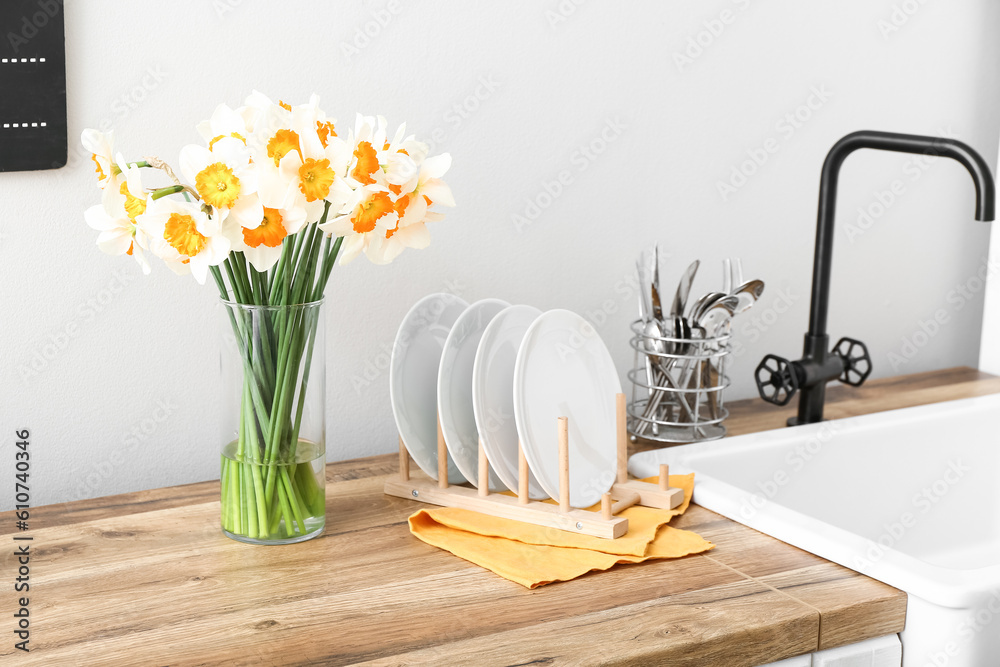 Vase with blooming narcissus flowers on wooden kitchen counter, closeup