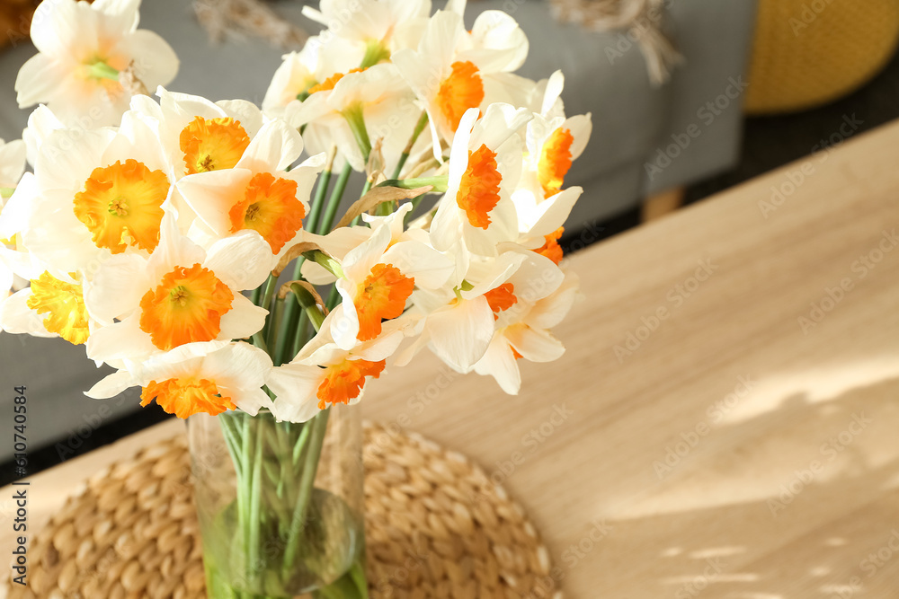 Vase with blooming narcissus flowers on table in light living room