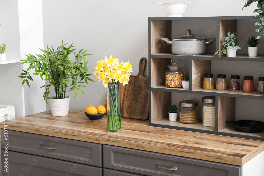 Vase with blooming narcissus flowers on counter in interior of kitchen