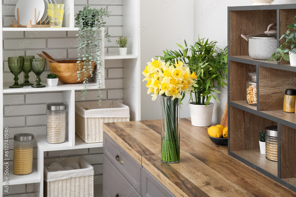 Vase with blooming narcissus flowers on counter in interior of kitchen