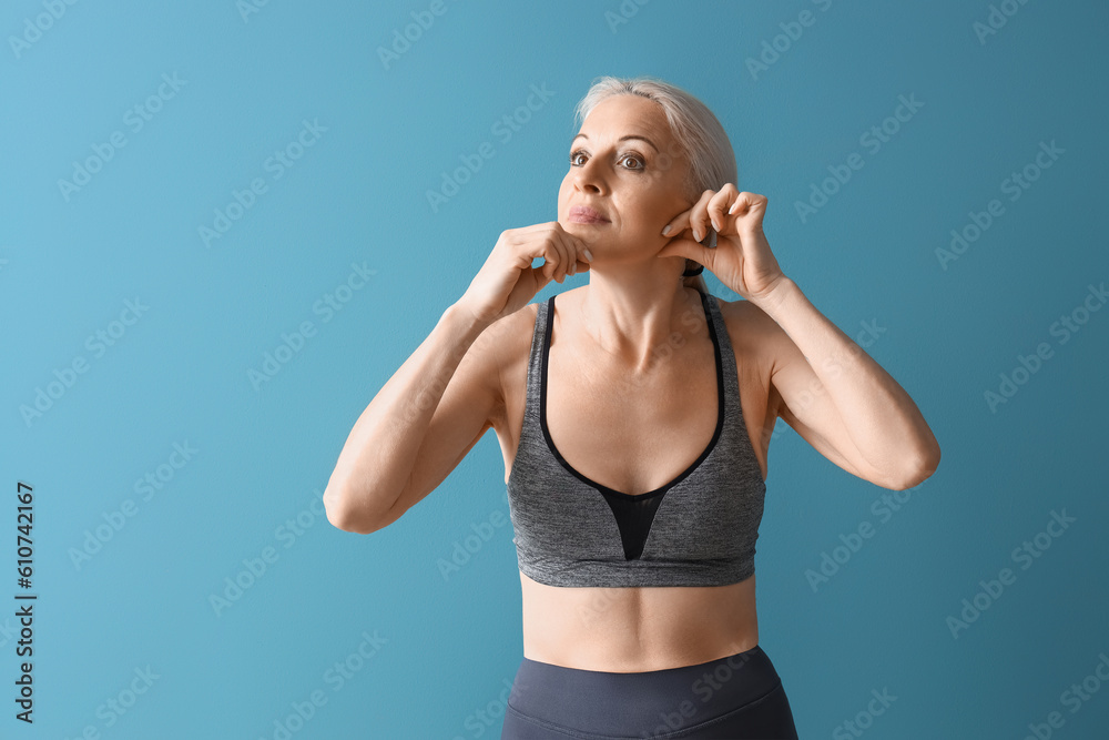 Sporty mature woman doing face building exercise on blue background