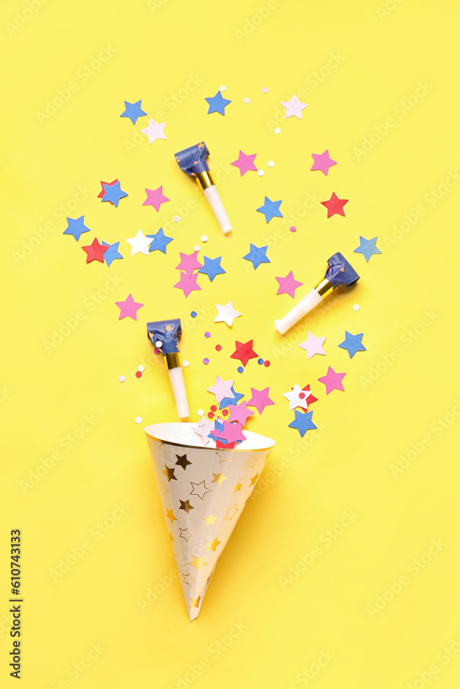 Composition with party hat and whistles on pale yellow background