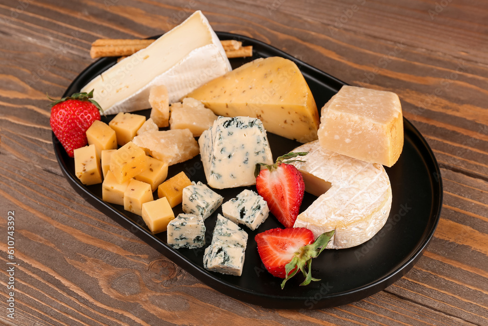 Tray with pieces of tasty cheese on wooden background