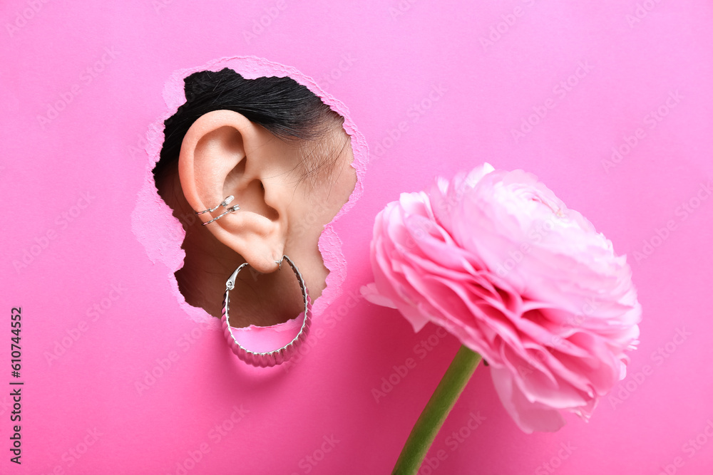 Ear of beautiful young woman with stylish earrings visible through torn pink paper