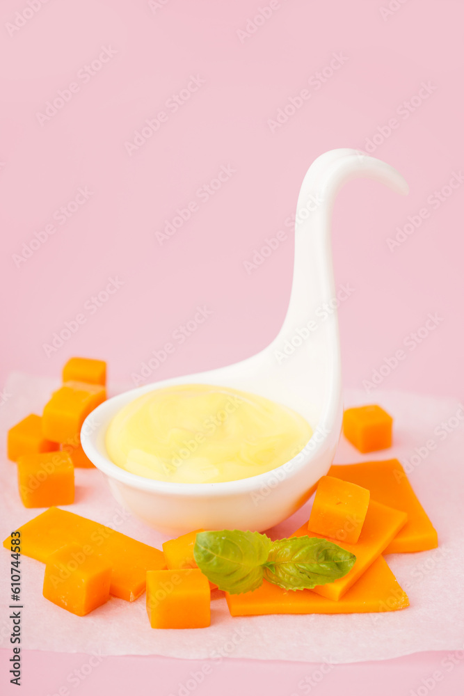 Bowl with tasty cheddar sauce and slices of cheese on pink background