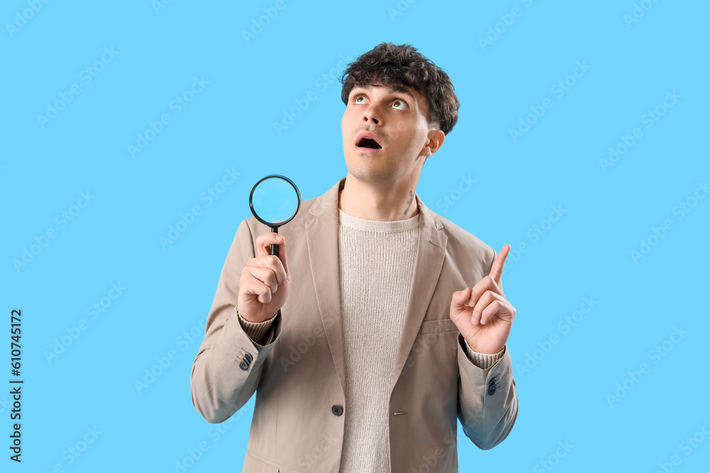 Young man with magnifier pointing at something on blue background