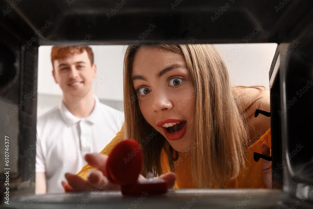 Happy young woman opening microwave oven with engagement ring, view from inside