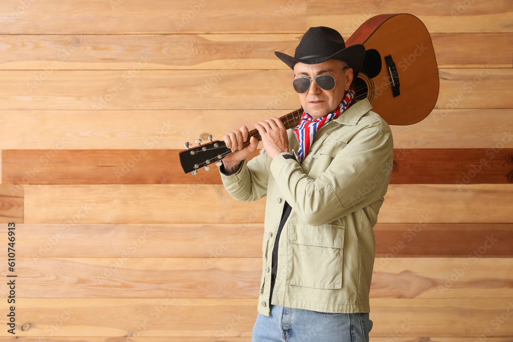 Mature cowboy with guitar on wooden background