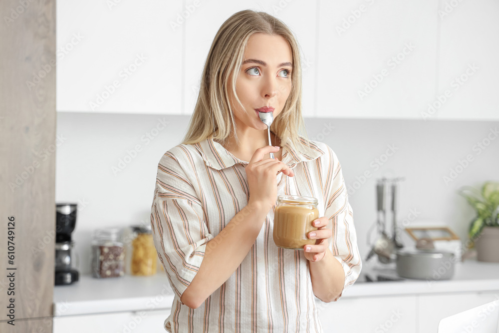 Young woman eating tasty nut butter in kitchen