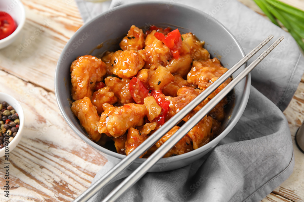 Bowl with tasty sweet and sour chicken on light wooden background, closeup