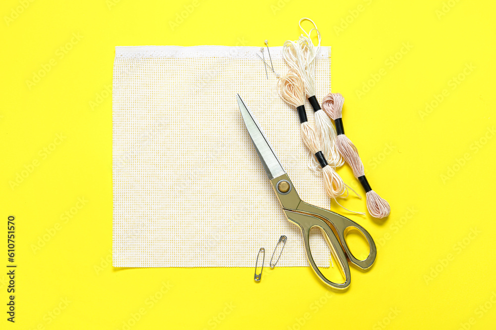 Canvas with scissors, mouline threads and pins on yellow background