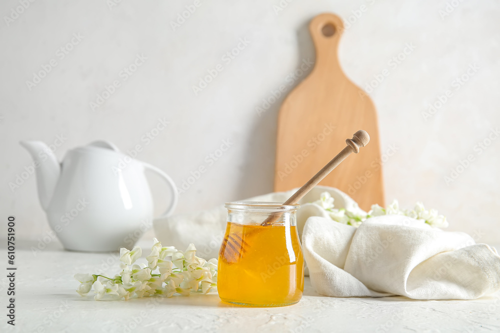 Jar of honey with flowers of acacia and teapot on light background