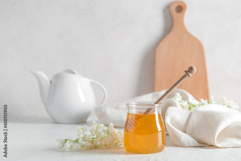 Jar of honey with flowers of acacia and teapot on light background