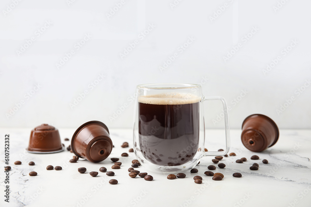 Cup of delicious coffee, pods and beans on white table