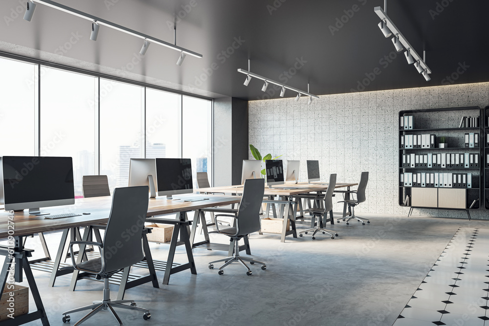 Open office interior with desks, computers, a concrete floor, and black ceiling. A window provides n