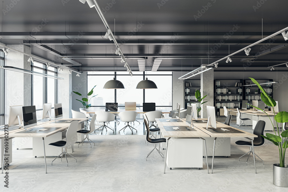 Front view of an open office interior with desks, computers, a concrete floor, and black ceiling. A 