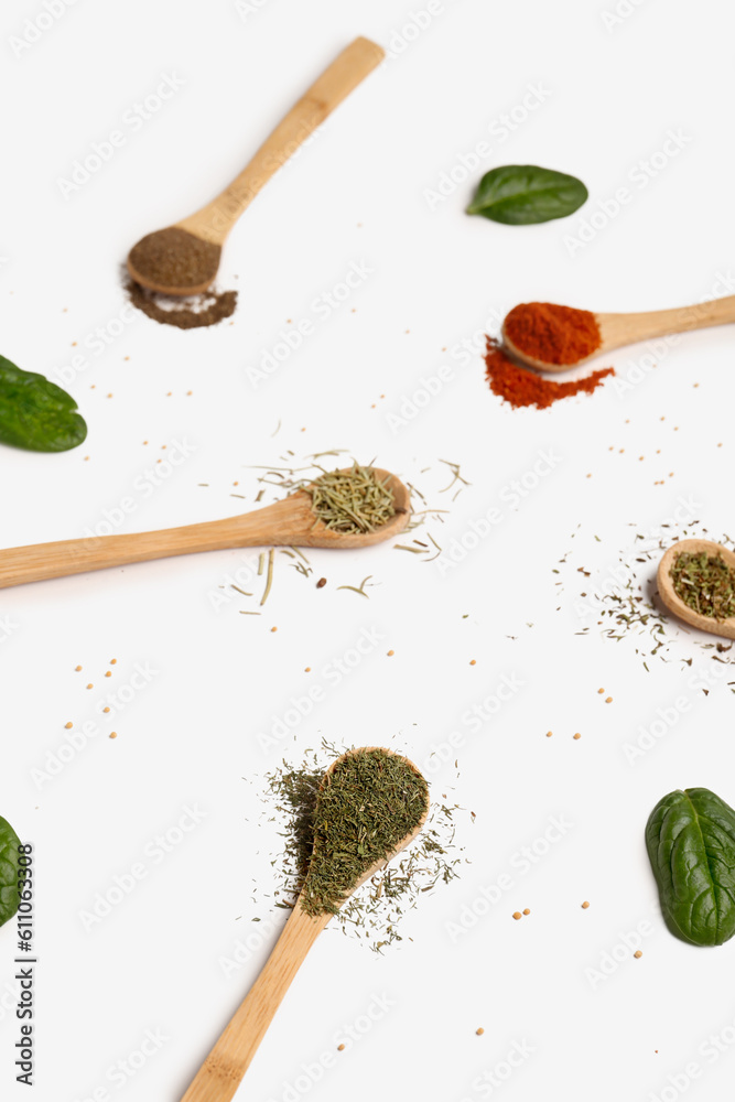 Composition with wooden spoons of aromatic spices and spinach leaves on light background