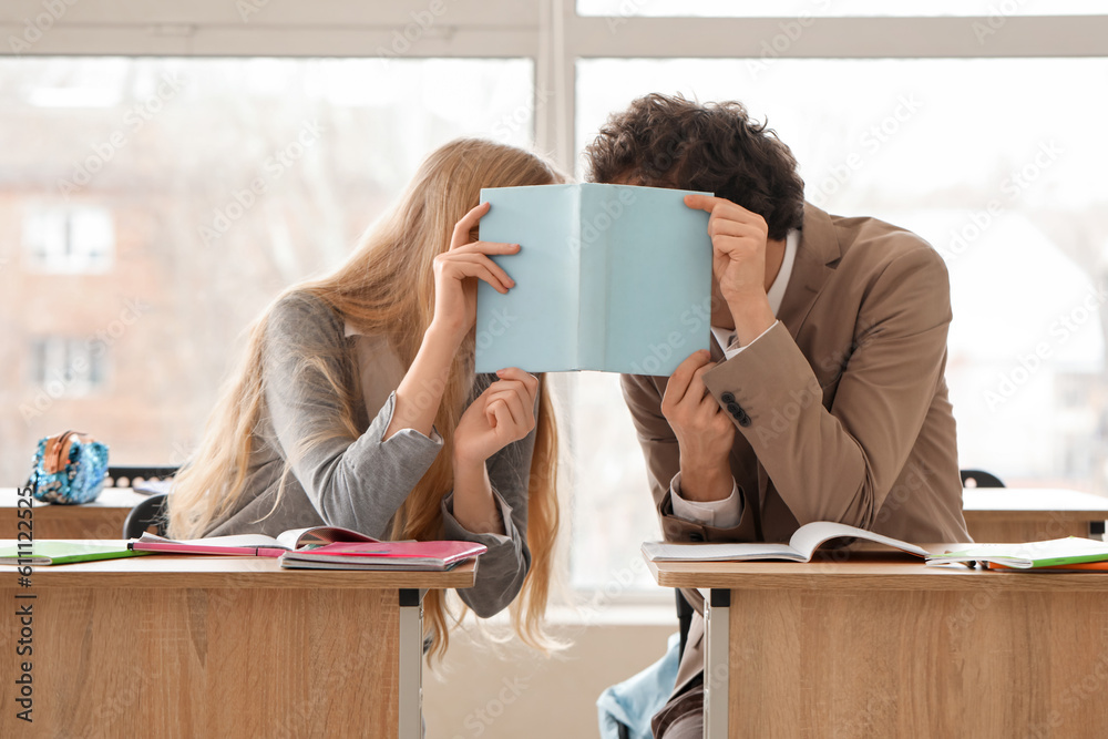 Teenage couple covering themselves with book in classroom