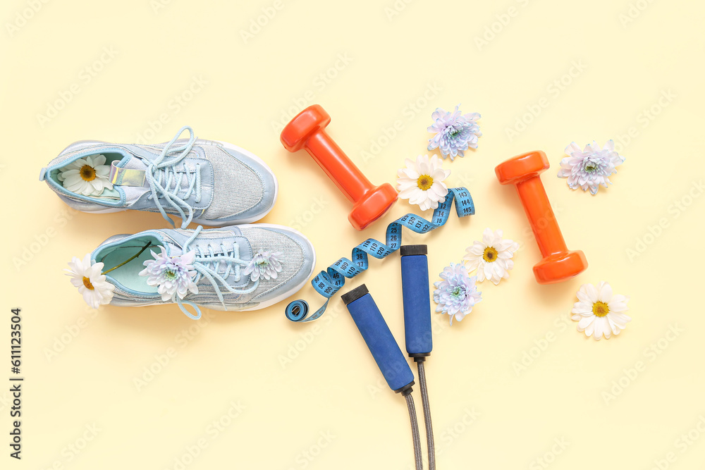 Sneakers with spring flowers, sports equipment and tape measure on beige background