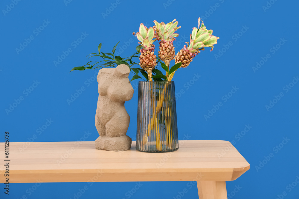 Vase with baby pineapples and decor on table near blue wall