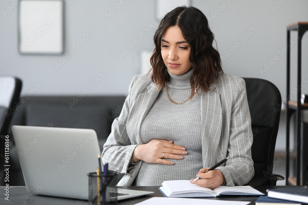 Young pregnant woman working at table in office