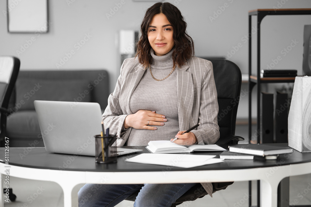 Young pregnant woman working at table in office