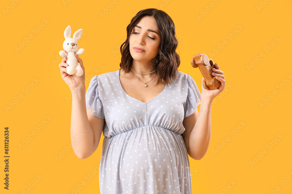 Young pregnant woman with baby toys on yellow background