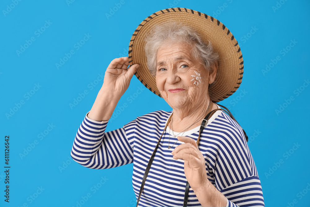 Senior woman with sun made of sunscreen cream on her face against blue background