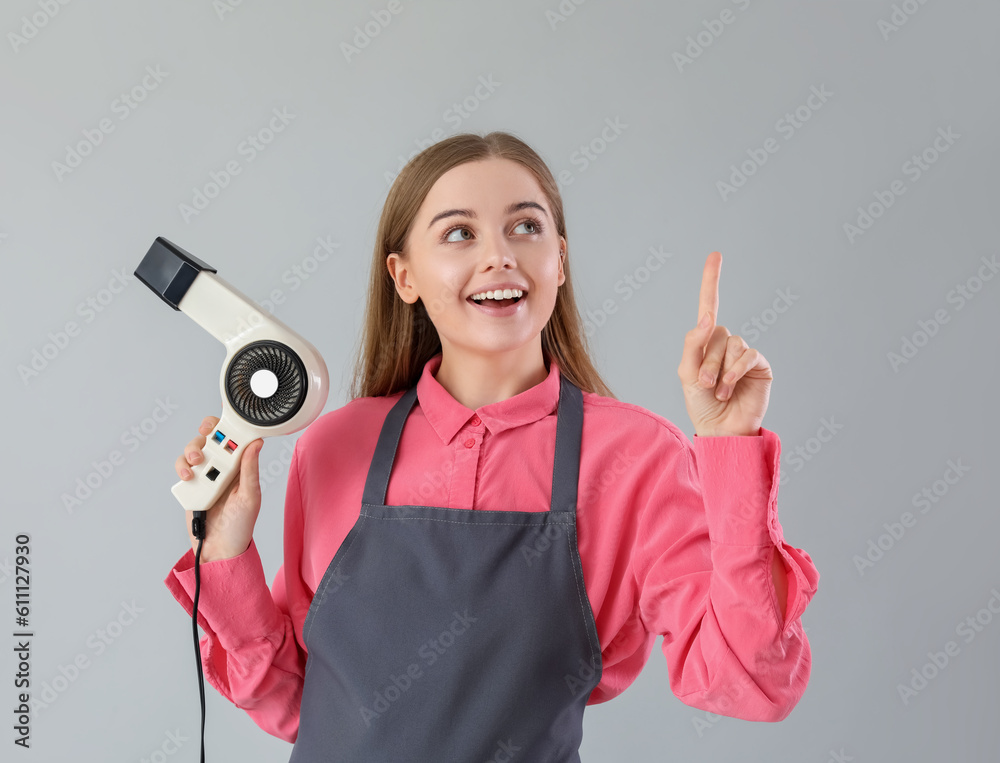 Female hairdresser with dryer pointing at something on grey background