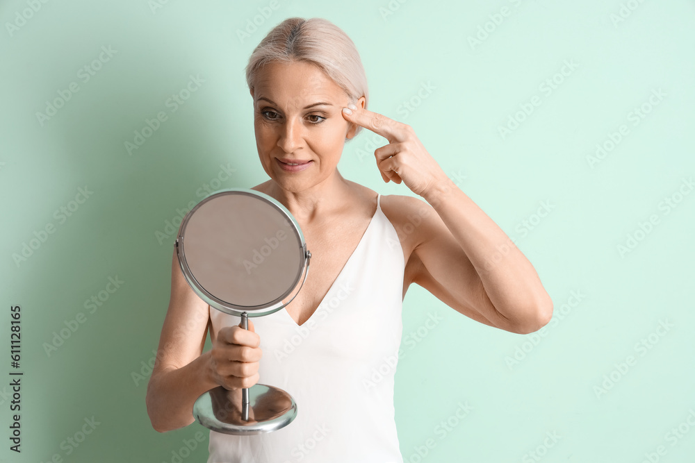 Mature woman with mirror doing face building exercise on green background