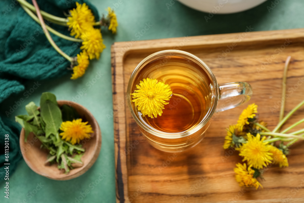 Board with glass cup of healthy dandelion tea on green background