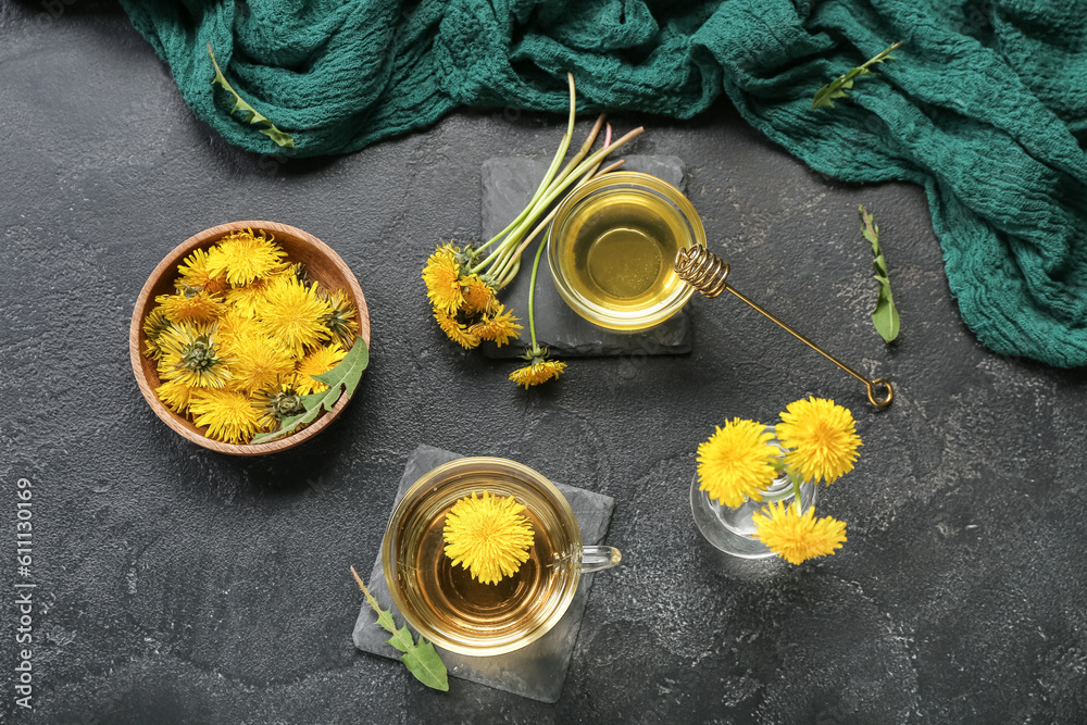 Glass cup of healthy dandelion tea and bowl with flowers on black background