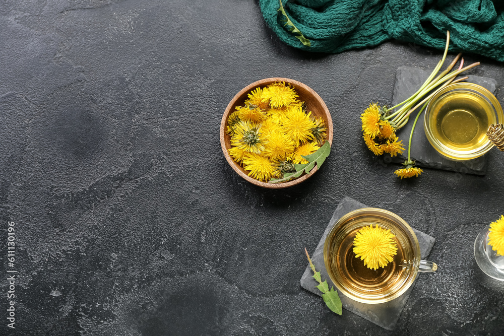 Glass cup of healthy dandelion tea and bowl with flowers on black background