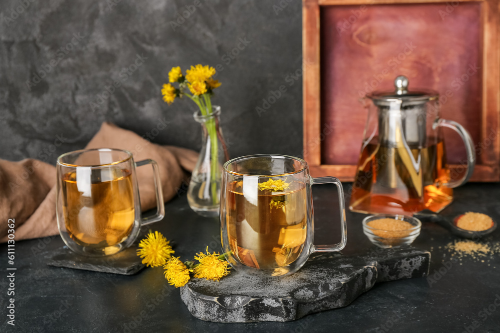 Board with glass cups of healthy dandelion tea and teapot on black table