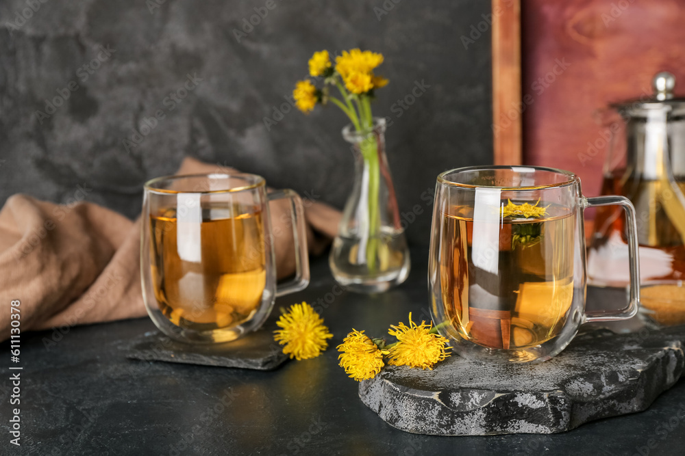 Board with glass cups of healthy dandelion tea and teapot on black table