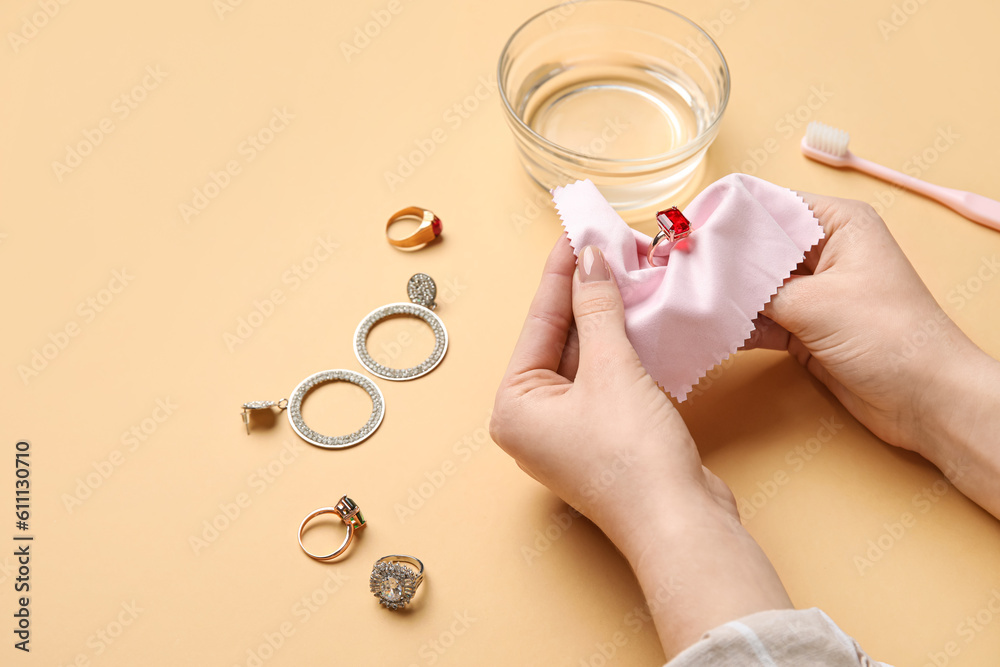 Woman polishing beautiful ring on color background, closeup