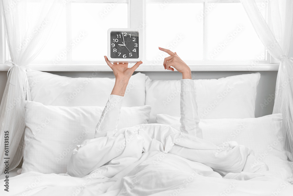 Morning of young woman pointing at clock in bed