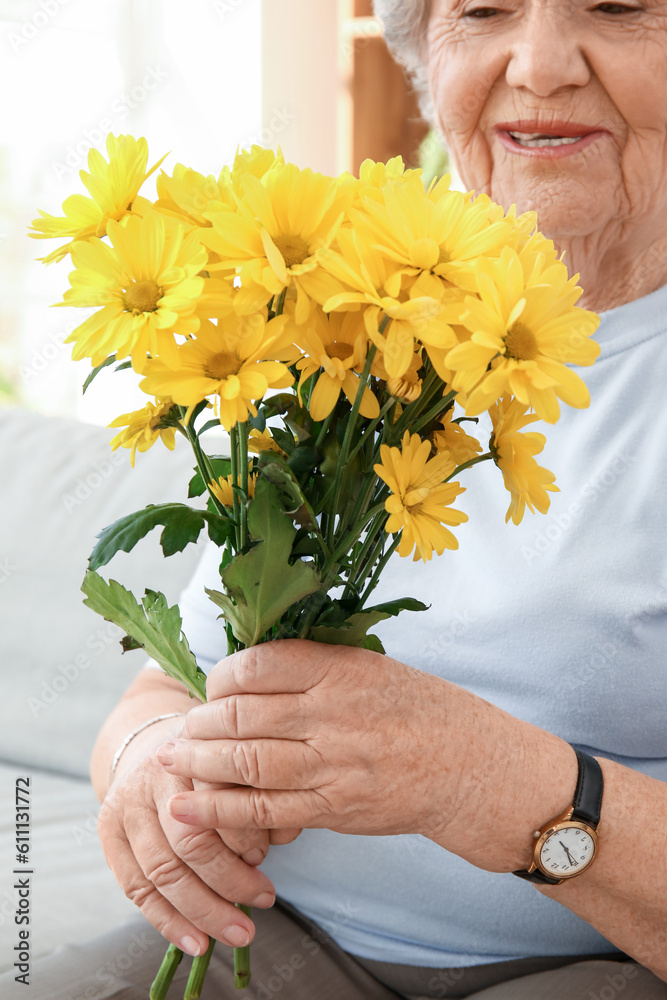 Senior woman with chrysanthemum flowers at home, closeup