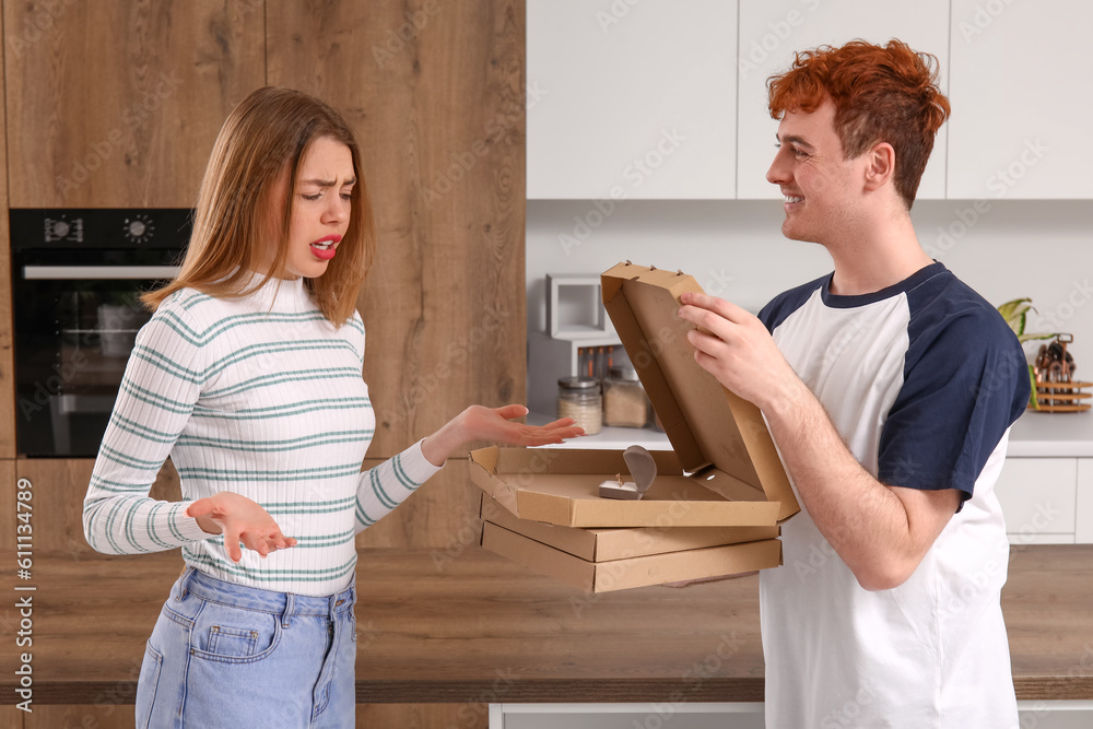 Young man with pizza proposing to his confused girlfriend in kitchen