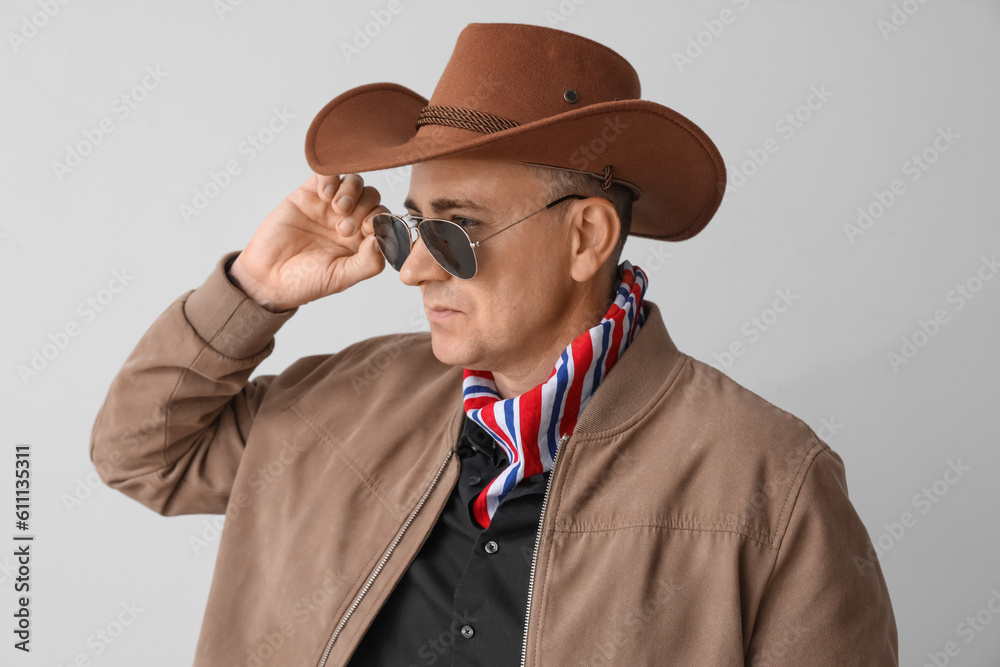 Mature cowboy in sunglasses on light background