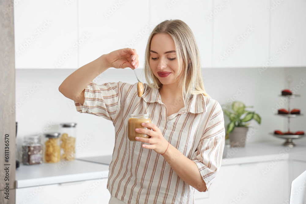 Young woman with spoon and jar of nut butter in kitchen